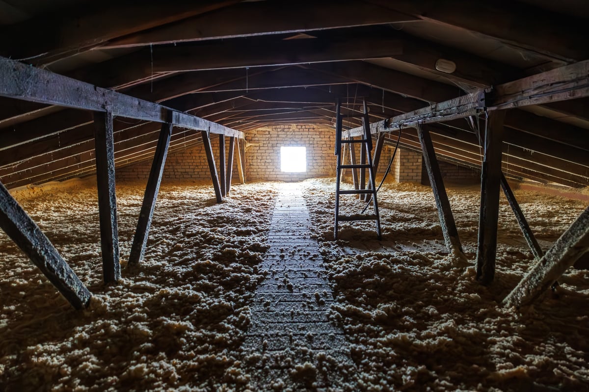 Attic space with insulation, plank walkway, wooden beams, and bright window