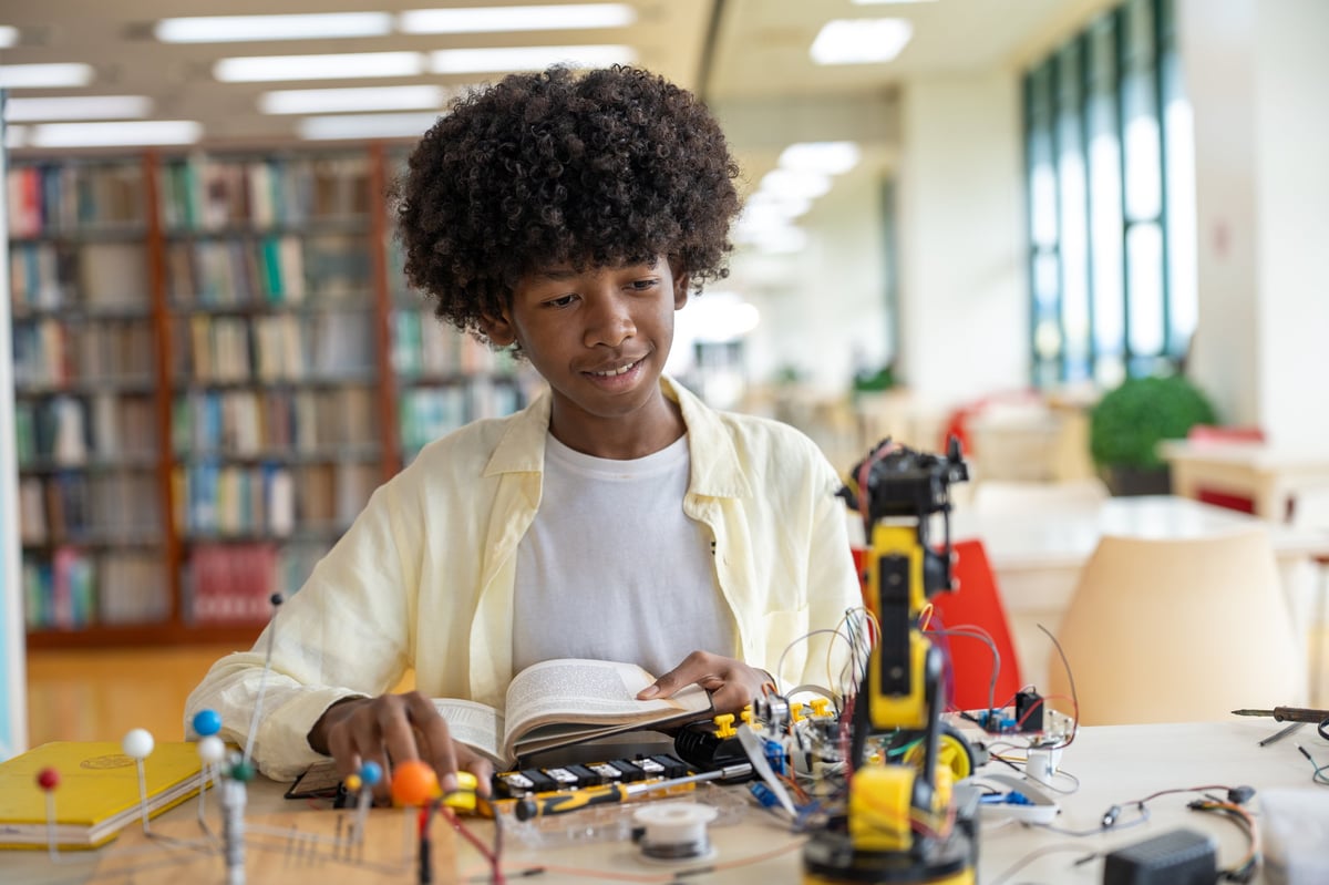 Aluno lendo e montando kit de robótica na biblioteca