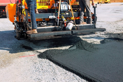 Workers operating paving machine laying new asphalt