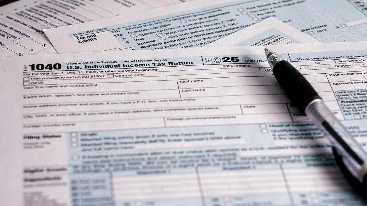 A person works on the U.S. individual income tax return for 2025. Tax forms and a pen are spread out on a table. The process involves filling out personal and financial details.