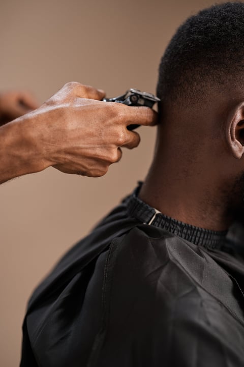 Young barber using electric clippers to trim the back of a client's neck