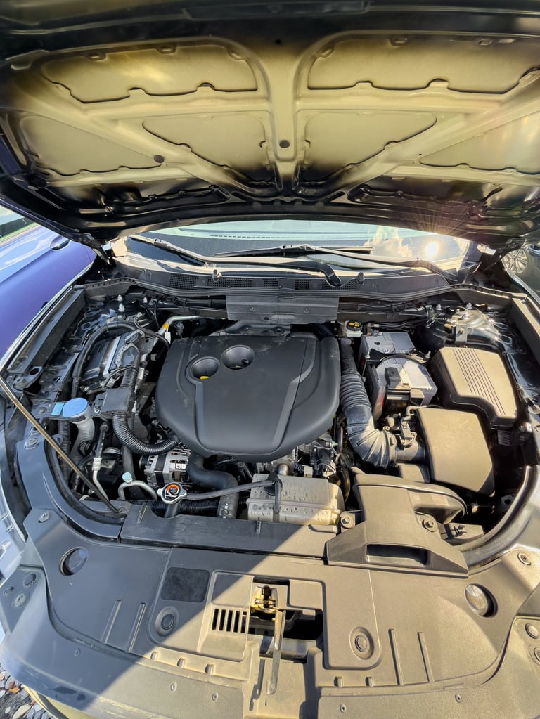 Under the hood of a modern car, various engine components are visible in bright sunlight. The engine bay highlights the intricate design and engineering beneath the surface.