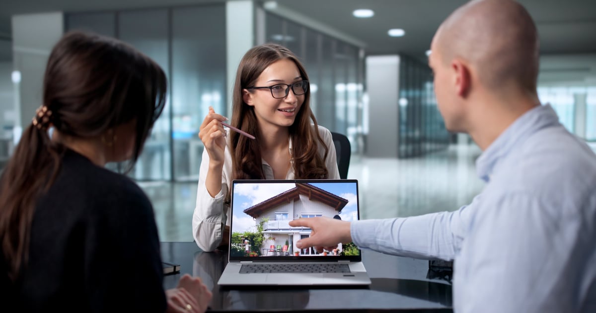 Asesora inmobiliaria profesional con clientes frente a una propiedad