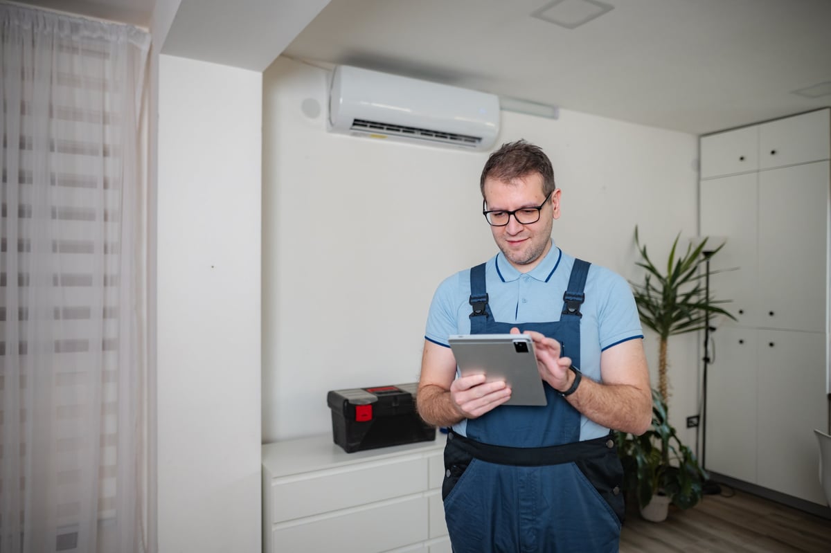 HVAC technician wearing overalls inspecting air conditioning and using a digital tablet