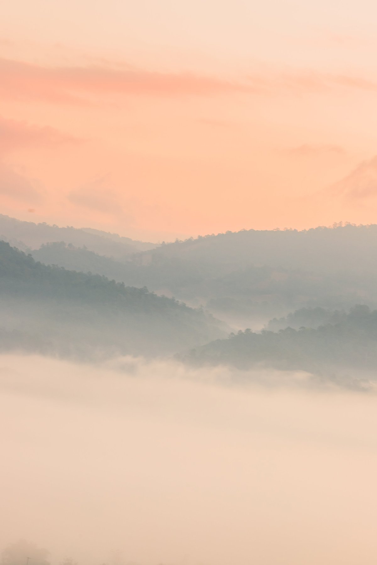 Serene layers of misty mountains beneath a soft pastel sunrise