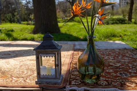 Elegant flowers in glass bottle with lantern on a rug — boho outdoor decor