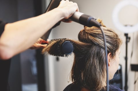 Hairdresser blow drying woman's hair with round brush