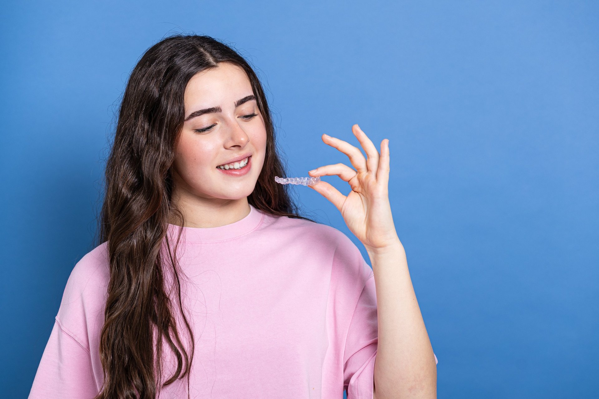 Young woman holding a clear Invisalign aligner tray and smiling