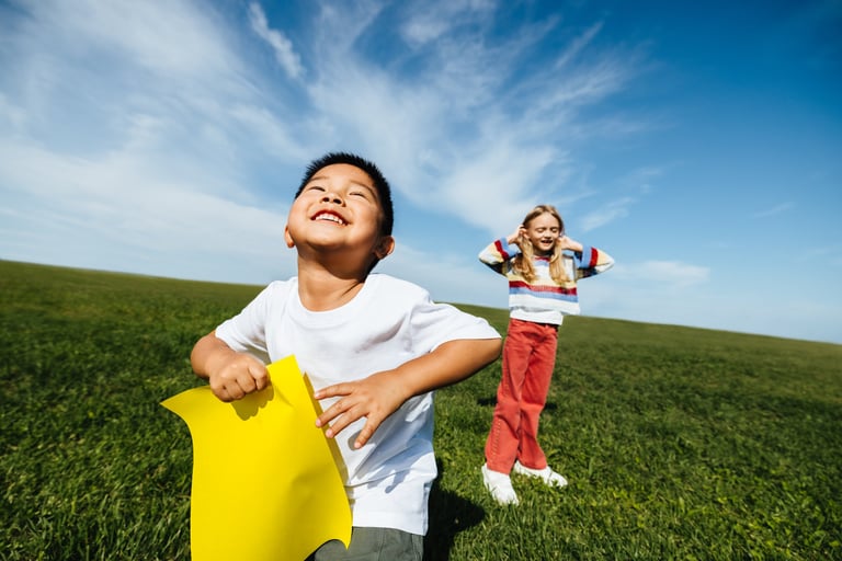 Two children laughing as they play in a wide grassy field on a bright summer day