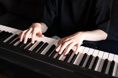 Mãos tocando um piano preto em close-up com iluminação suave