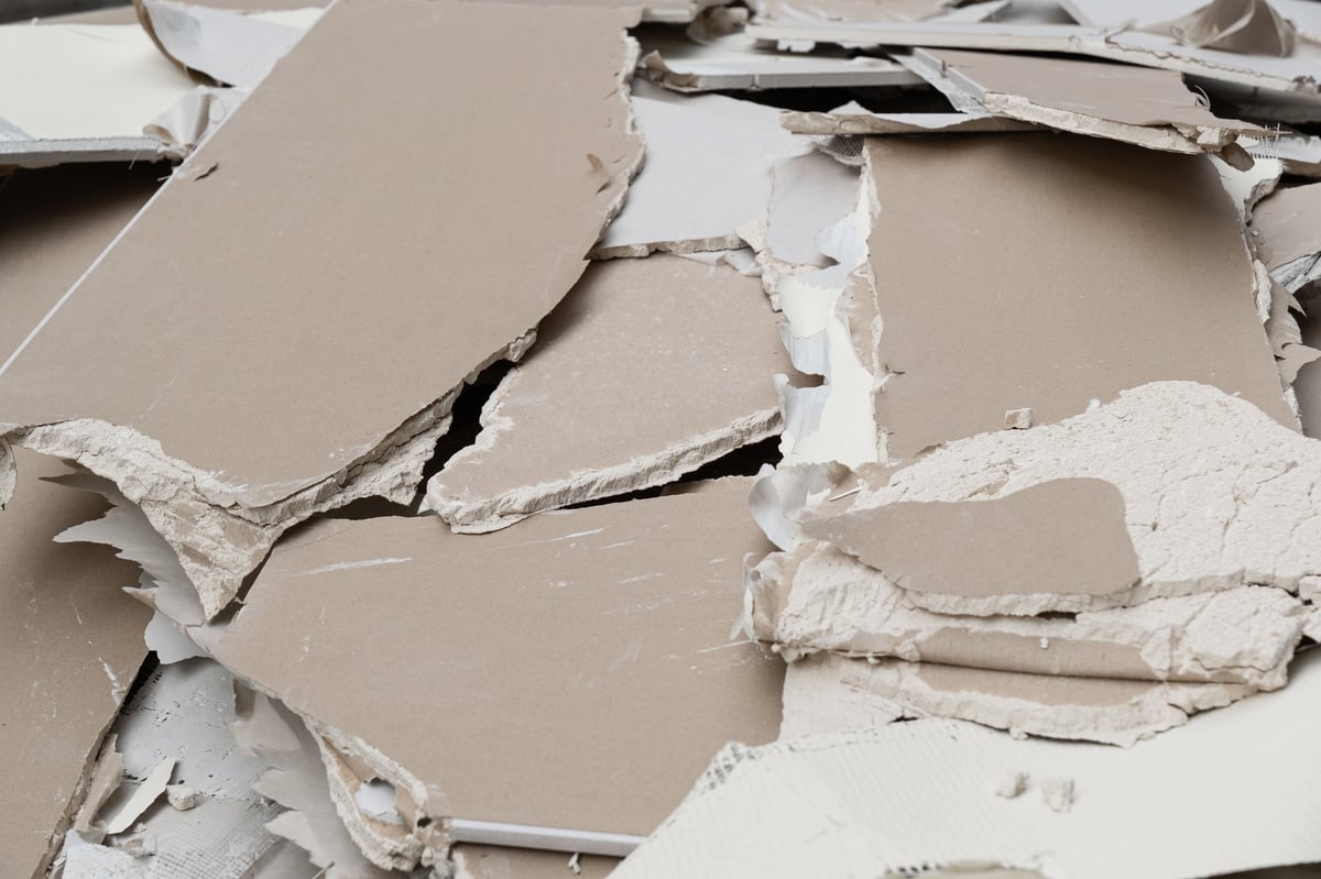 Large fragments of torn drywall and gypsum boards showing paper layers and mineral core