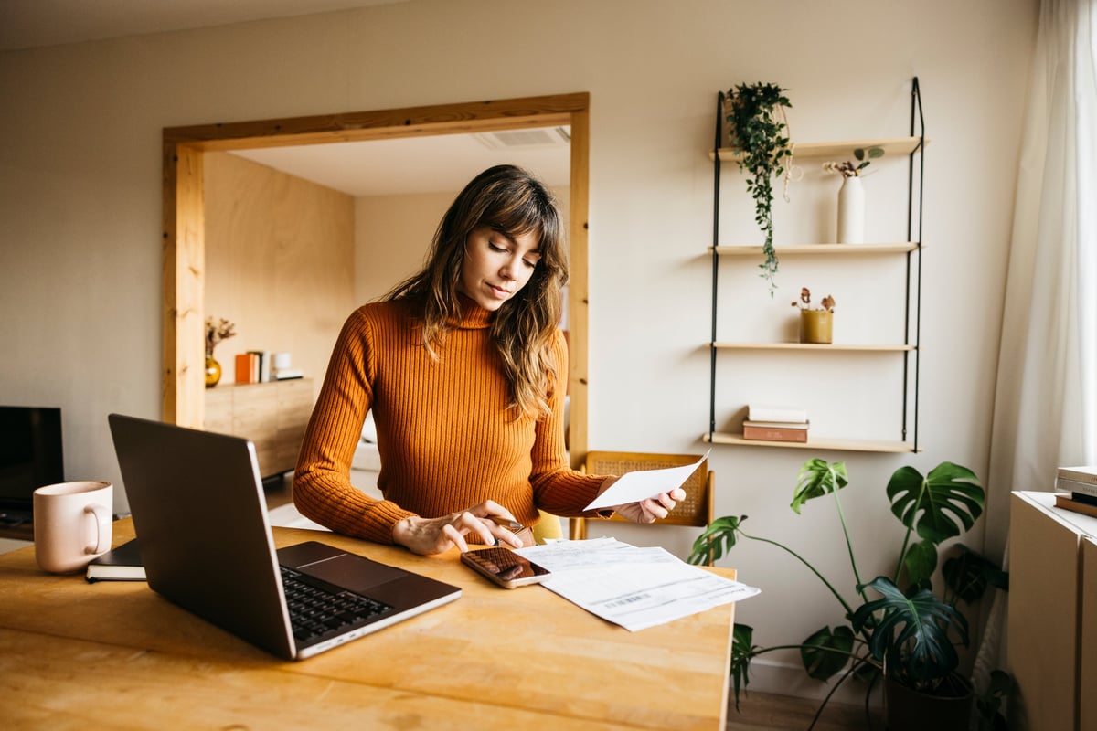 Self-employed business owner reviewing expenses and income on a laptop at a home office