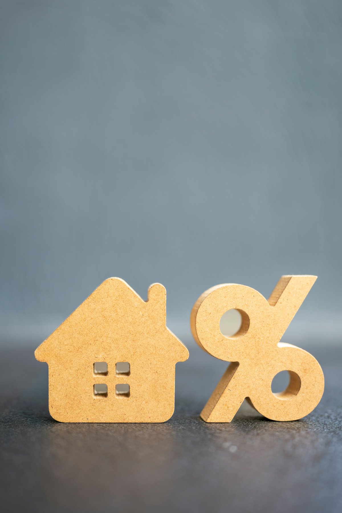Wooden house model next to percentage symbol representing mortgage interest rate and property finance