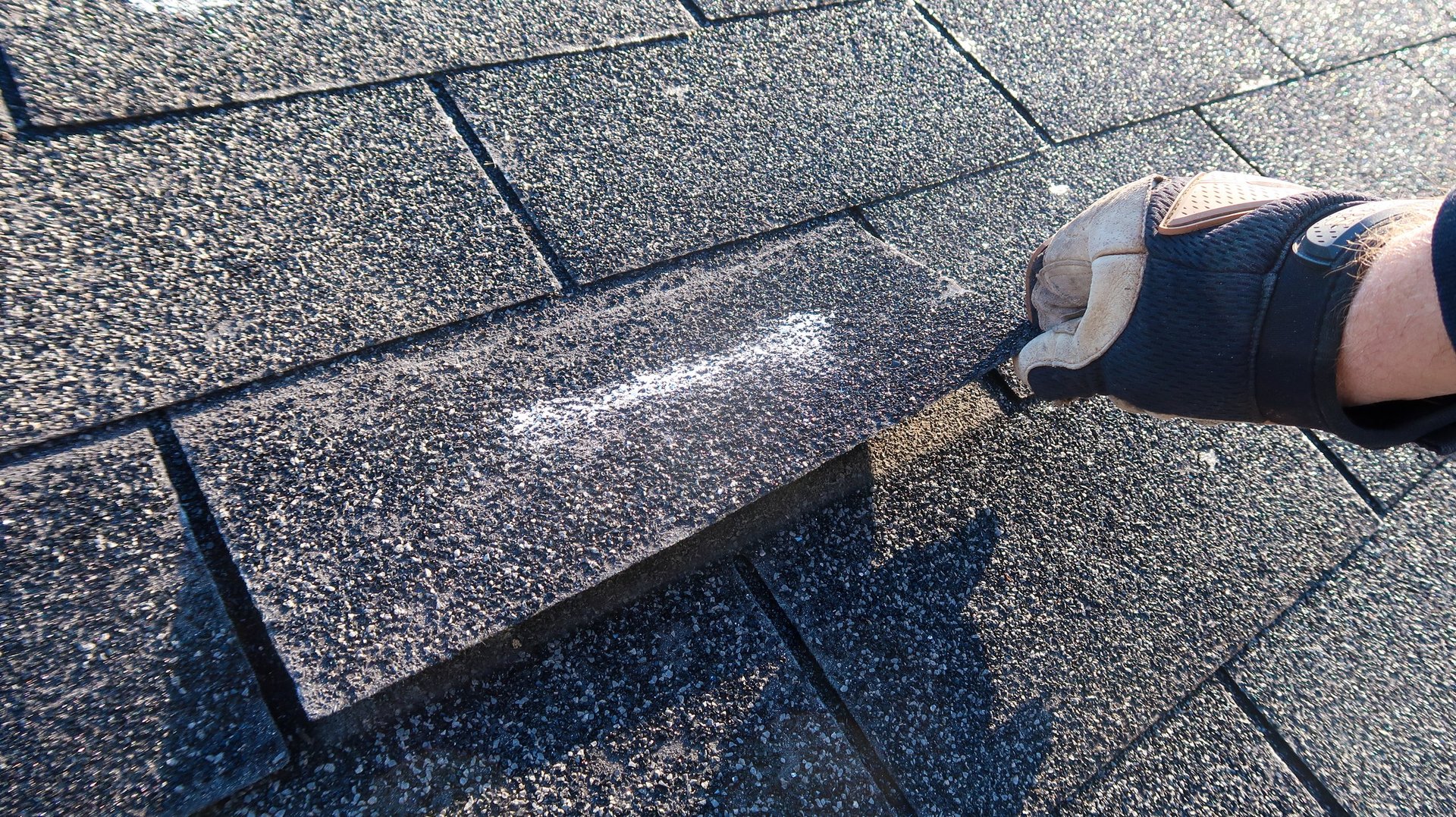 Roofing professional performing a hands-on maintenance check, lifting a shingle to inspect for wind damage