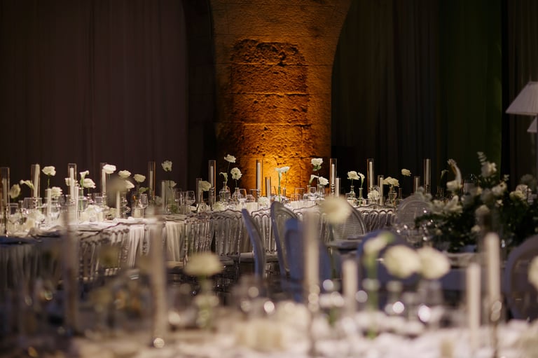 Elegant wedding reception tables with white floral details and candles in a historic stone hall