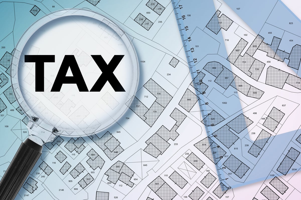PROPERTY AND LAND TAX CONCEPT WITH MAGNIFYING GLASS OVER CADASTRAL MAP, REAL ESTATE TAXATION, LAND REGISTRY ANALYSIS, HOUSING COSTS, FINANCIAL BURDEN, GOVERNMENT TAX INCREASE, PROPERTY VALUATION
