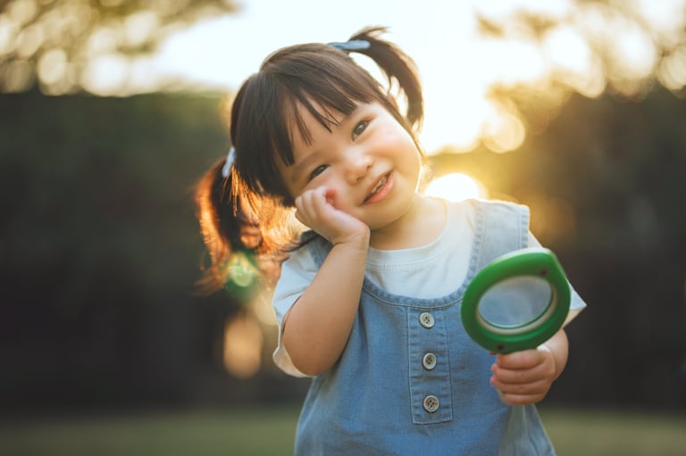 A happy little Asian girl holding a toy magnifying glass while exploring plants outdoors