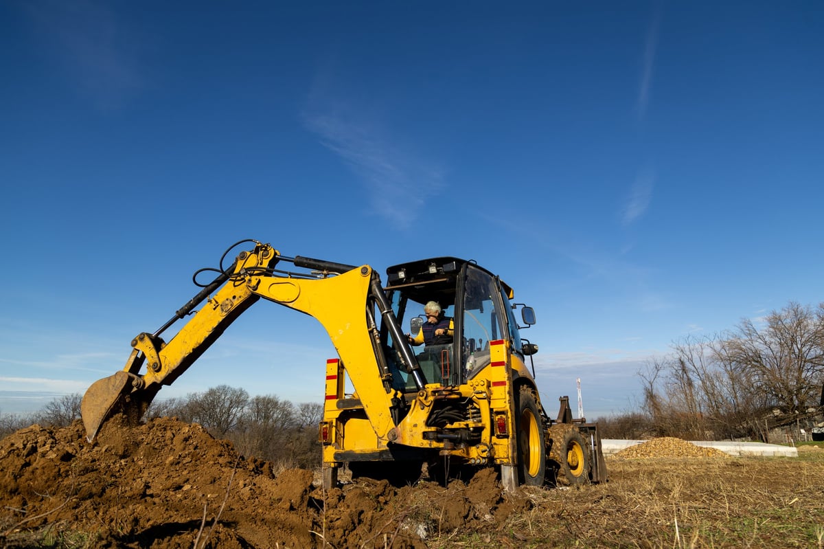 A yellow backhoe loader excavating soil on a construction site under a clear sky