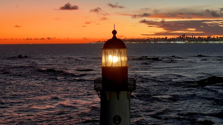 A coastal lighthouse standing over a calm shoreline at sunrise