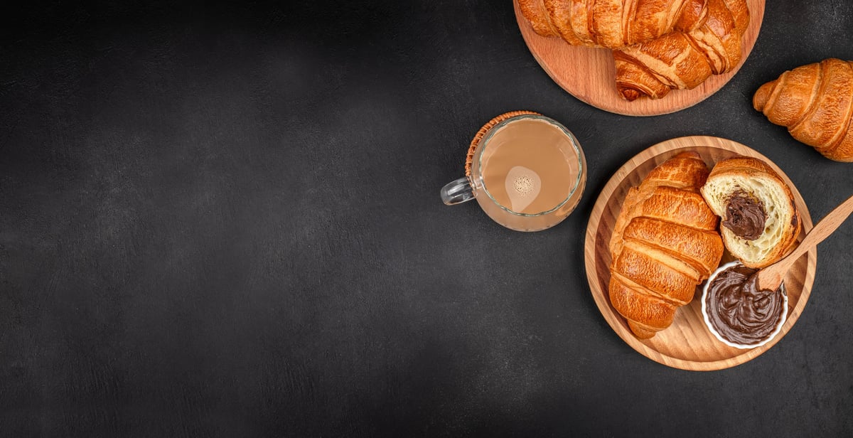 Frische Croissants mit Schokolade und Kaffee auf dunklem Holztisch