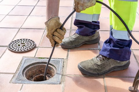 Sewer worker unclogging blocked yard drain with high pressure water jetting