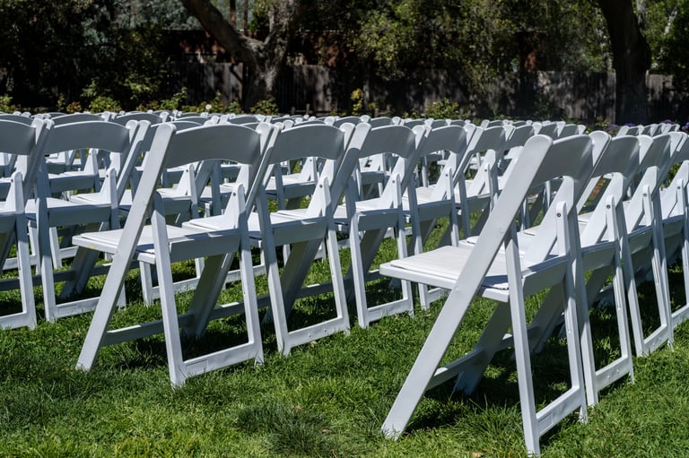 Rows of white chairs set up in a grassy area for a ceremony