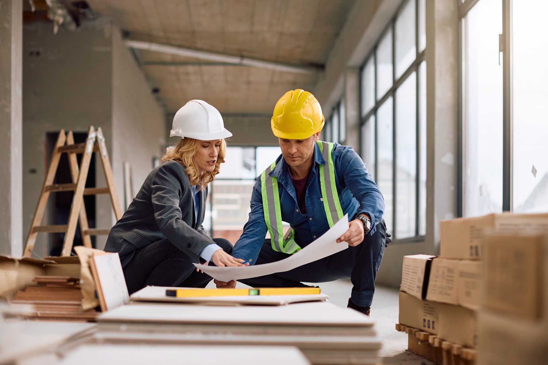 Construction worker and female real estate developer cooperating while examining construction plans at building site