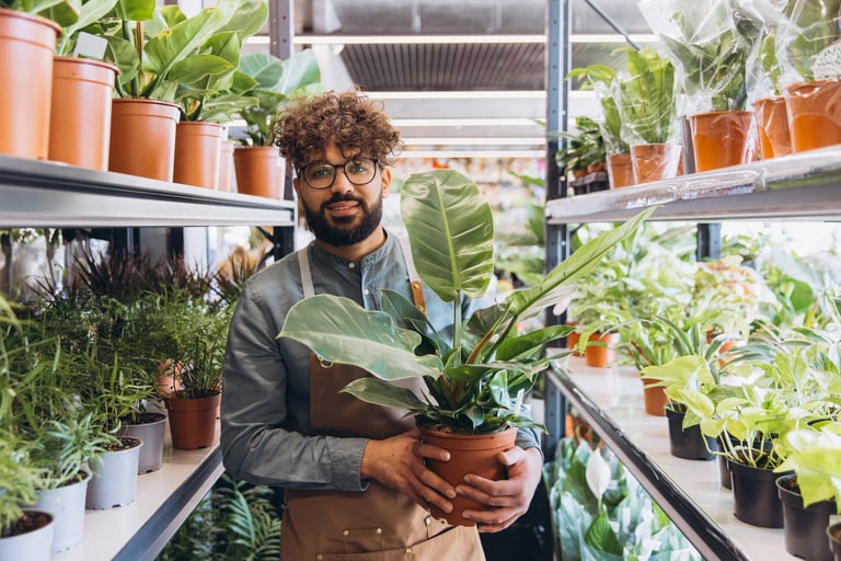 Happy male florist holding a green plant in a nursery