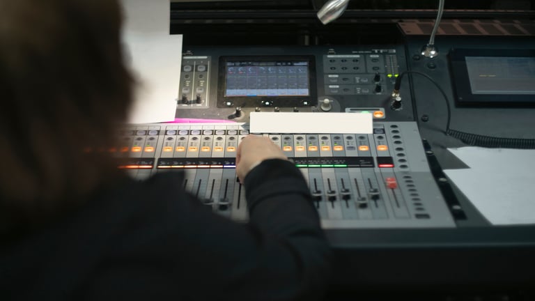 Audio engineer at mixing console — hands on faders, over-the-shoulder shot