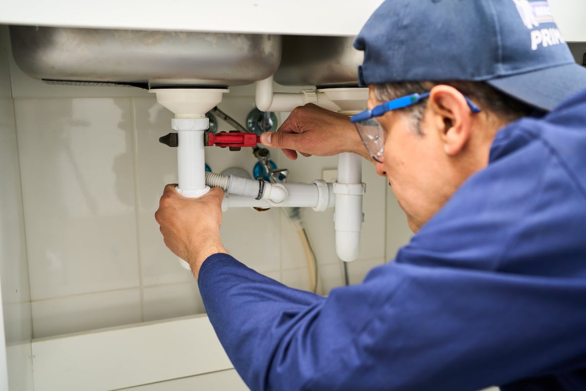 A plumber fixing a sink in a kitchen, with pipes and tools on show