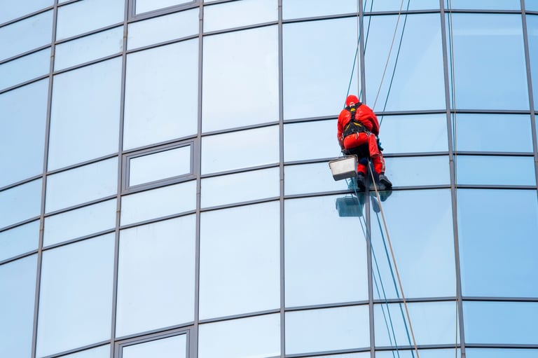 Worker cleaning windows on tall glass building