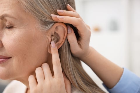 Woman putting hearing aid into her mother's ear at home