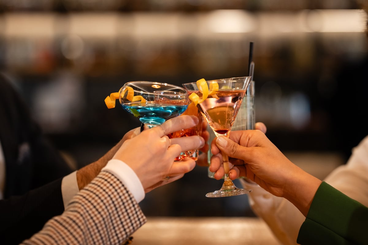 Many hands holding refreshing cocktails, making a toast and celebrating together during an evening social gathering at a bar