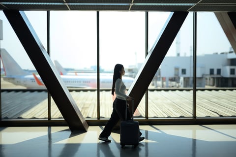 Traveler walking with suitcase past airport window and airplane