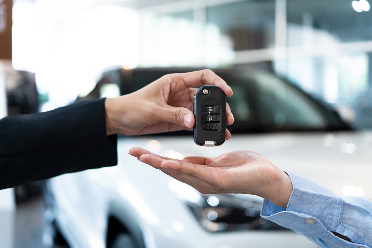 Car dealer handing over a key to a customer in a showroom