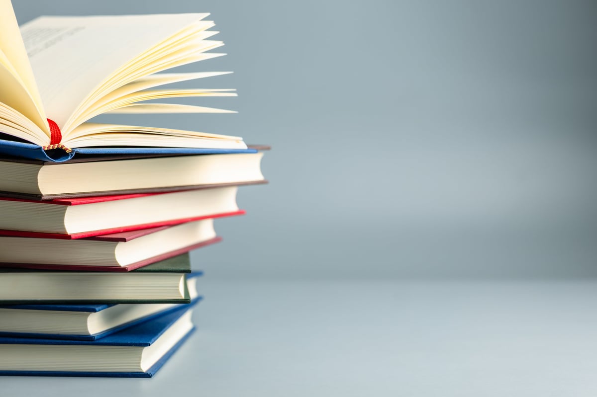 An open book resting on a stack of hardcover books against a minimal background