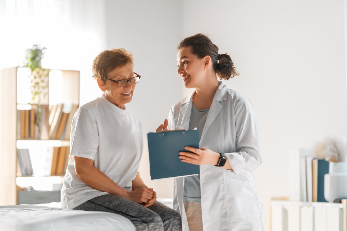 Healthcare coordinator providing geriatric care management for elderly parent — warm healthcare interaction showing a female doctor consulting a senior woman in a modern medical office