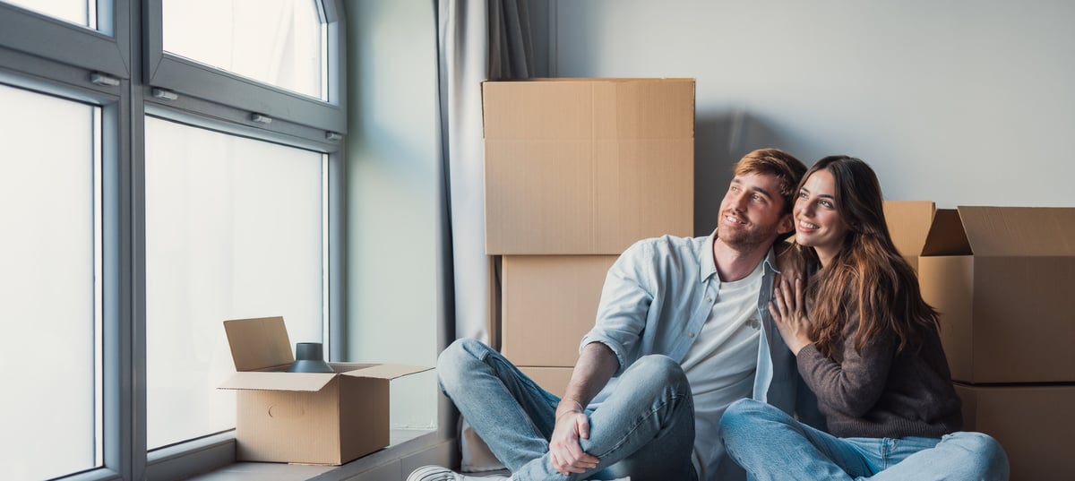 Young couple sitting in their new home surrounded by boxes, planning their financial future