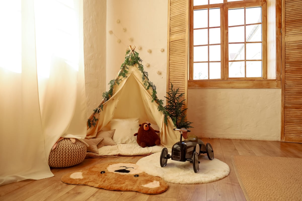 A cozy play tent with plush toys inside, a soft rug, and natural light from a window — a peaceful calm-down corner