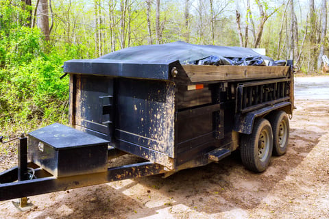 Black roll-off dumpster trailer on dirt road