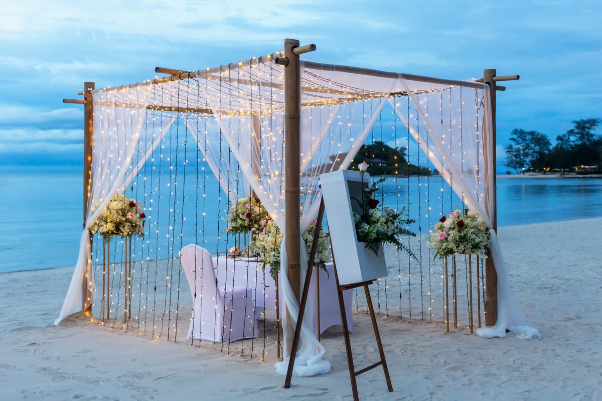 Beautifully decorated romantic proposal canopy with florals, fairy lights, and a dreamy sunset backdrop