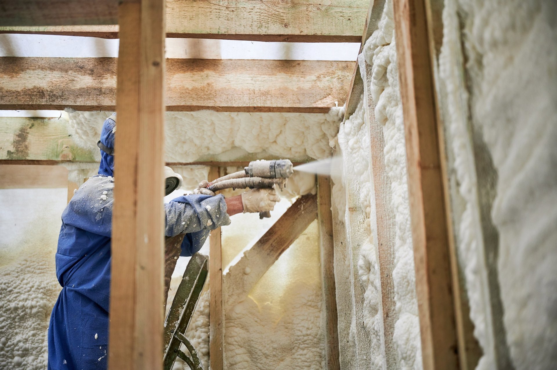 Worker applying polyurethane foam insulation to overhead timber cavity