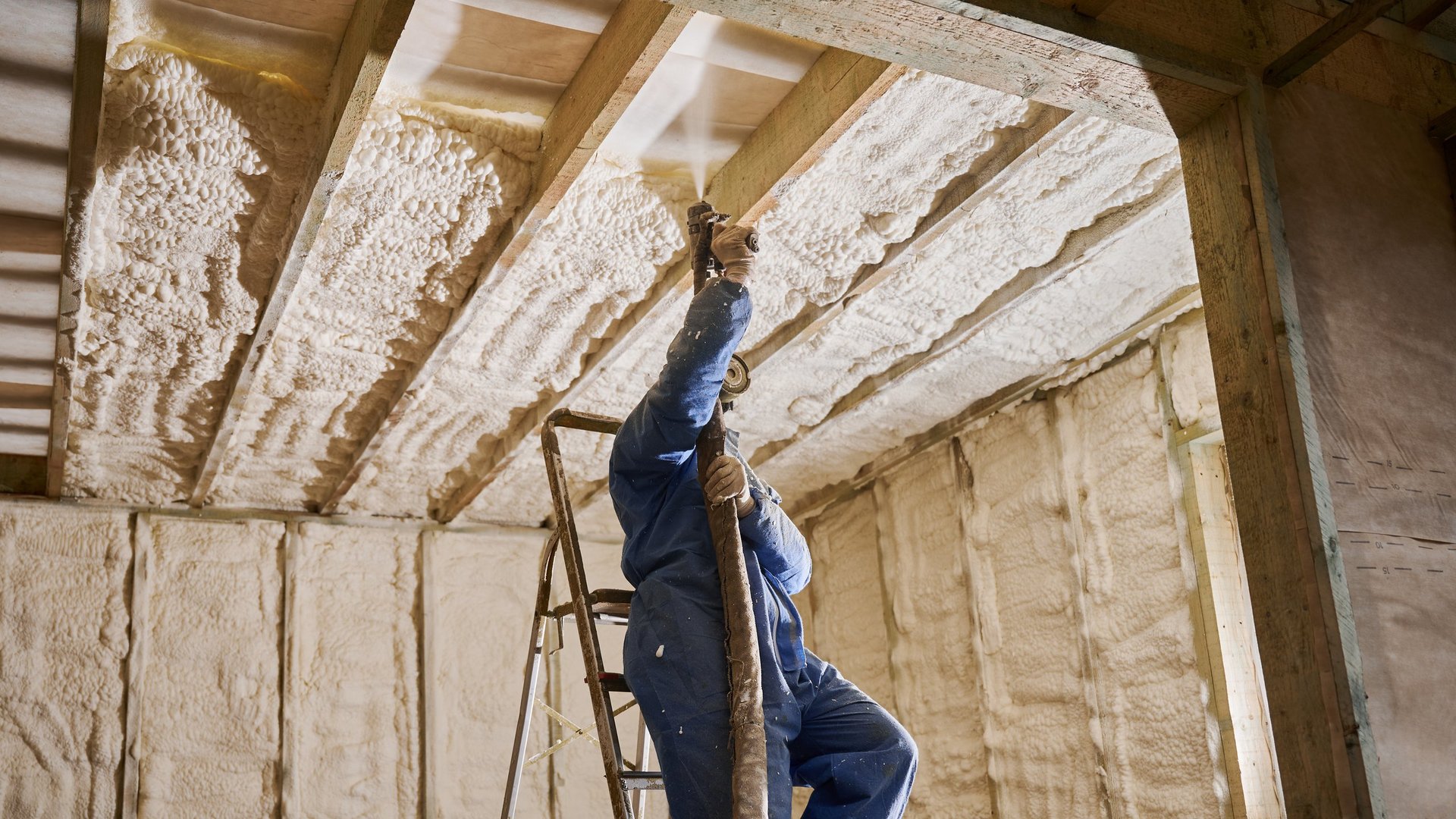 Builder applying spray foam insulation to ceiling structure
