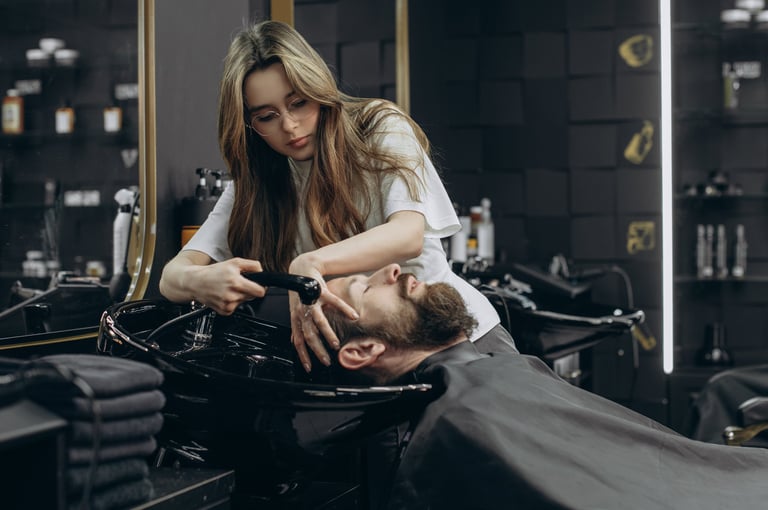 Female barber washing hair of bearded man at salon sink