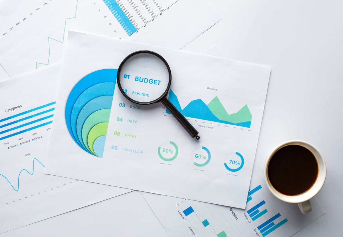 Printed charts and graphs with magnifying glass and laptop corner. Concept of business analytics, market research, and data visualization.