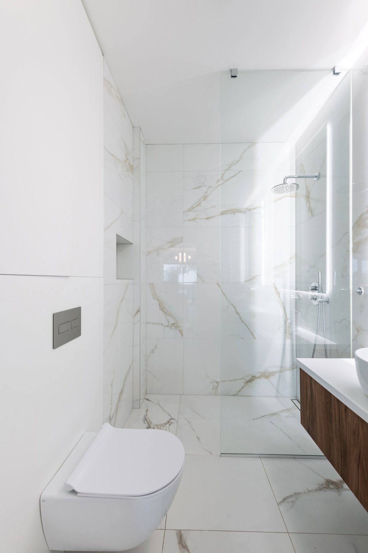 Bright modern bathroom with white marble tiles frameless walk-in glass shower
