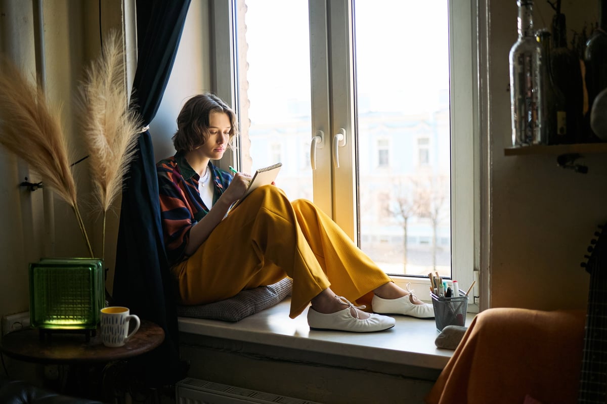 A young woman in her twenties writing in a notebook by a bright window, the way cycle tracking works