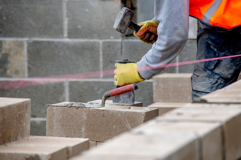 Construction worker placing bricks with hammer and trowel on building site
