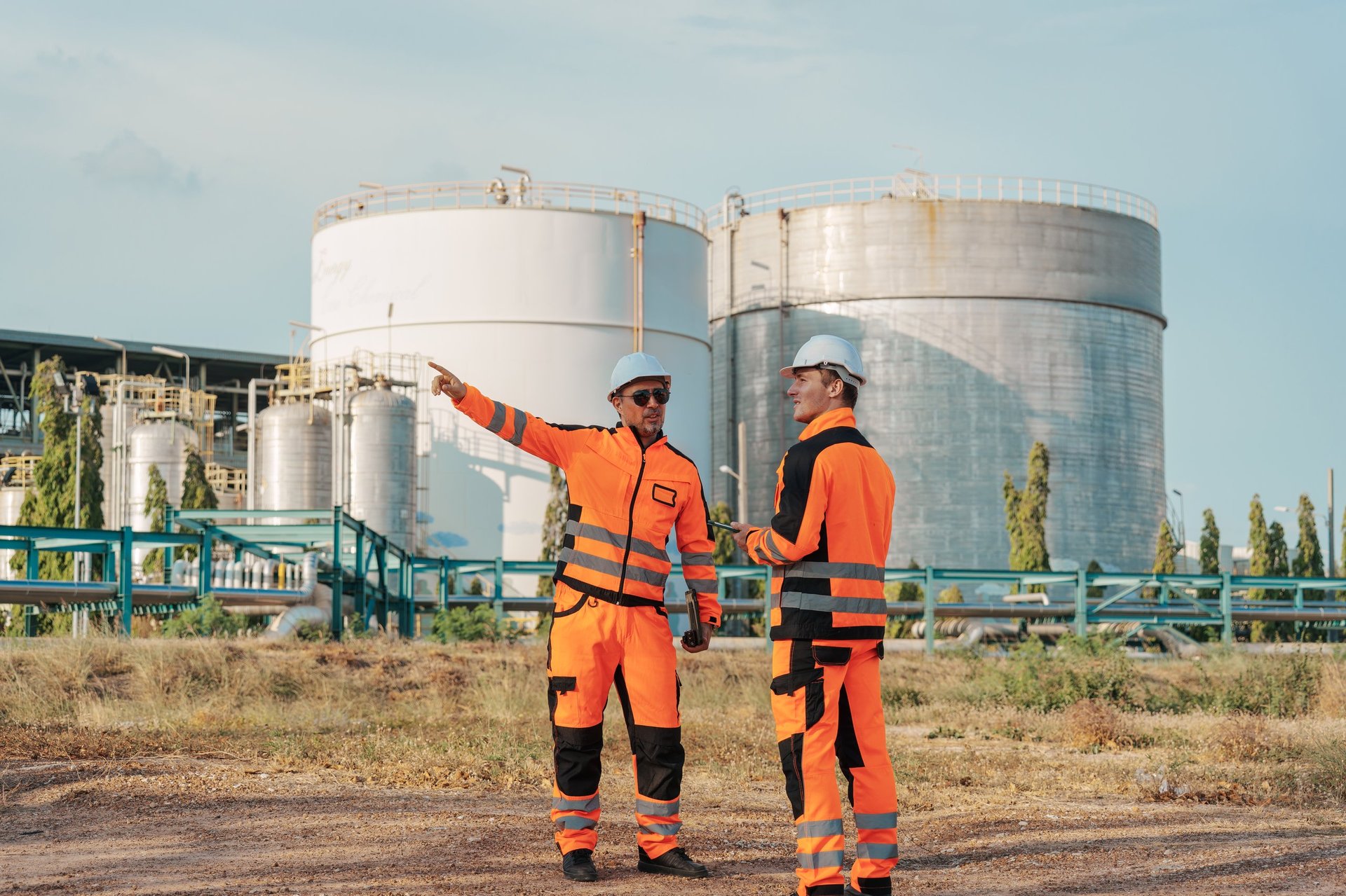 Two petrochemical engineer men at oil refinery factory with large storage tanks