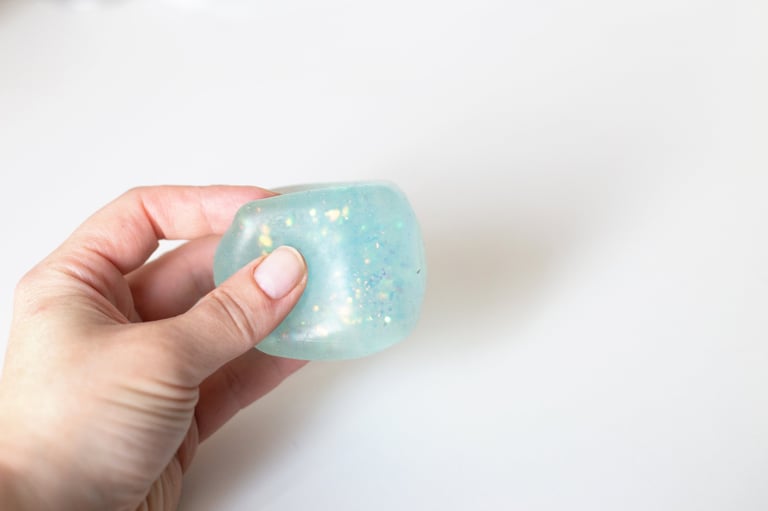 Hand deforming a light blue squishy toy with glitter against a white background